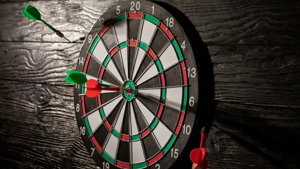 Green and red darts stuck in a classic dart board on a dark wooden wall.