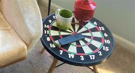 Round dart board table with cup and remote next to a chair.