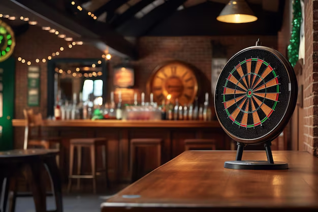 Miniature dart board on a wooden bar counter in a cozy pub with string lights.