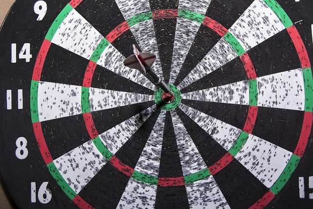 Close-up of a dart board with a dart perfectly hitting the center bullseye.