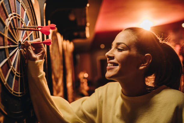 Happy woman smiling while placing a dart into the vibrant dart board.