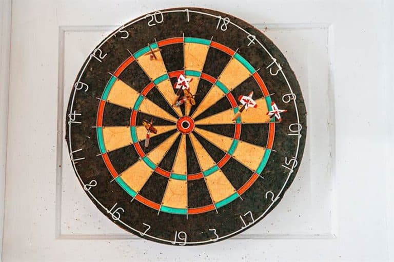 Dart board mounted on a white door with several darts, ready for play.