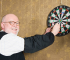 Smiling man collecting darts from a dart board, looking happy.