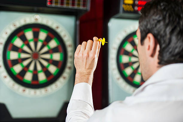 Man preparing to throw a dart at a dart board in a bar setting.