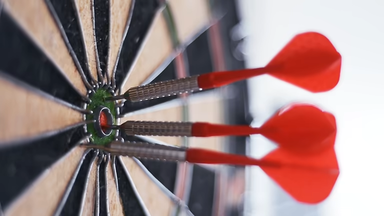 Three red darts precisely hit the bullseye of a classic dart board.