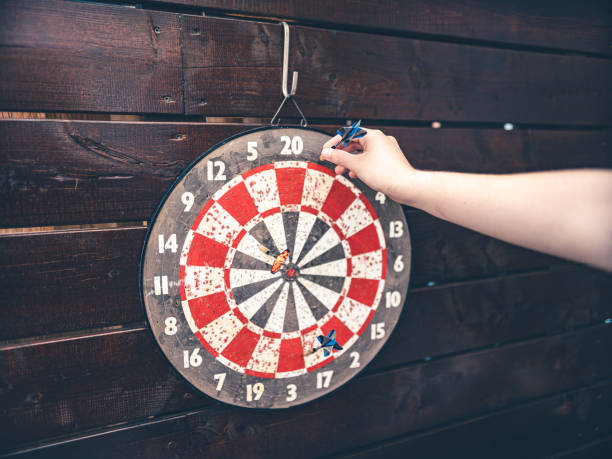 Hand removing a dart from a red and white dart board on a wooden wall.