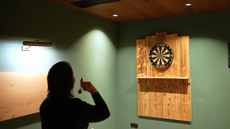 Person aiming a dart at a traditional dart board on a wooden wall.