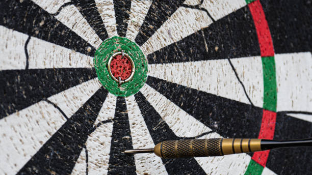 A metal-tipped dart sticks in a worn-out dart board, close to the bullseye.