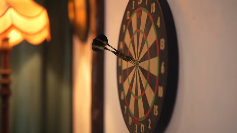 Two black darts firmly stuck in a classic dart board on a home wall.
