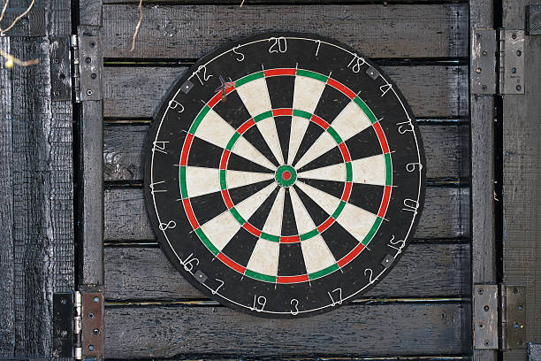 A dart board with one dart, mounted on rustic dark wooden planks outdoors.