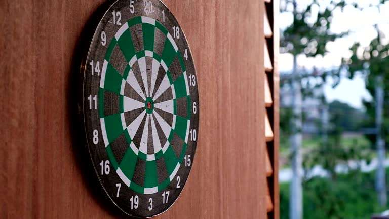 Green and black dart board mounted on a wooden wall with an outdoor background.
